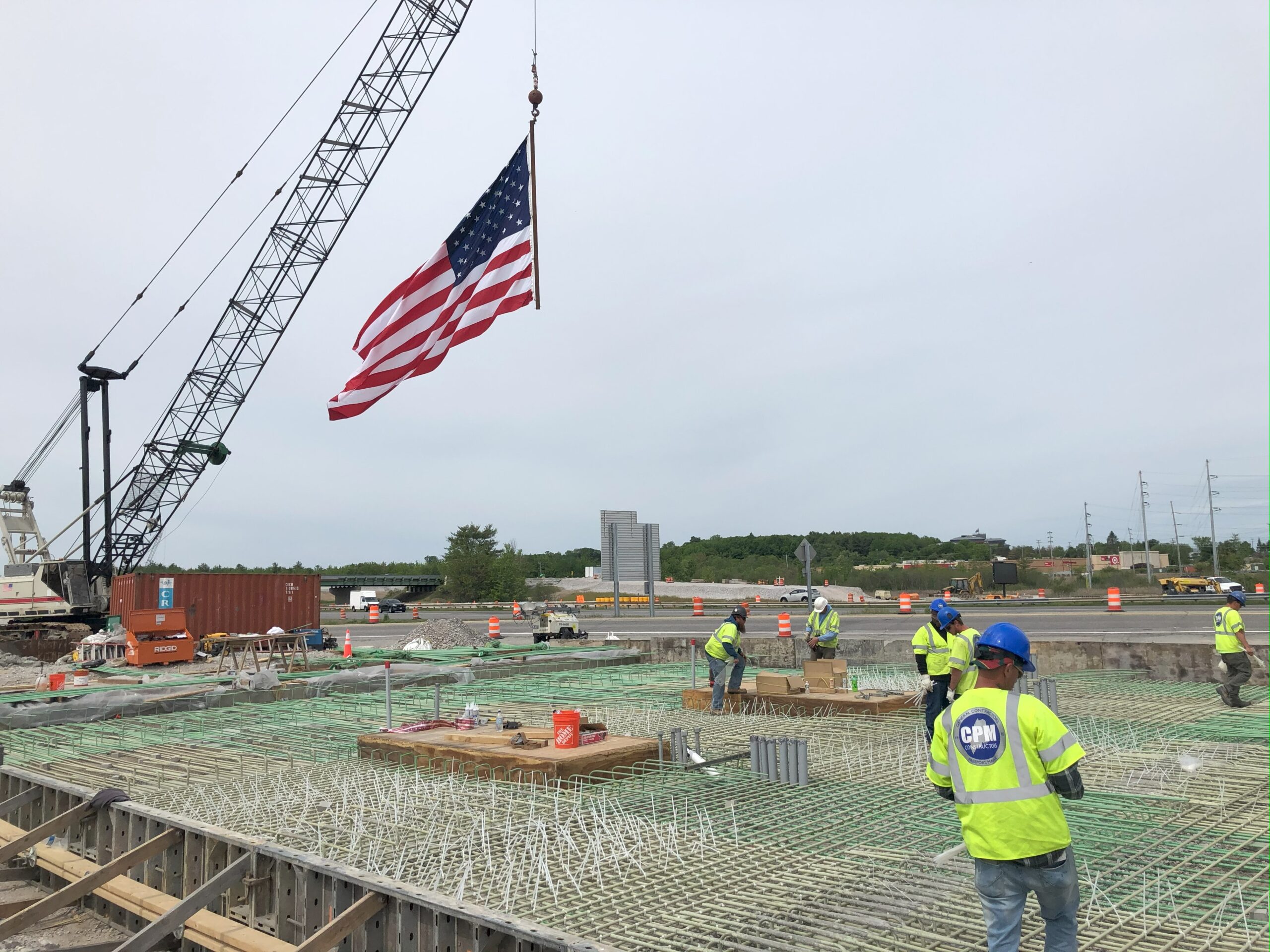Picture of workers on CPM Constructors Northbound Toll Plaza project in the rebar phase. A crane arm waves an American Flag. 